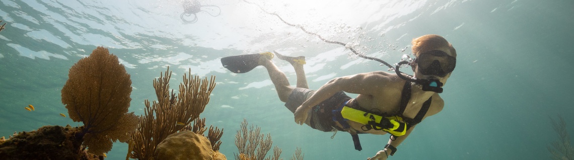 Diver exploring an underwater reef using the BLU3 Nomad battery-powered dive system, connected by a hose to the surface unit floating above.